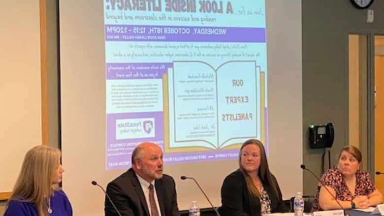 3 females and 1 male sit on a panel inside a classroom